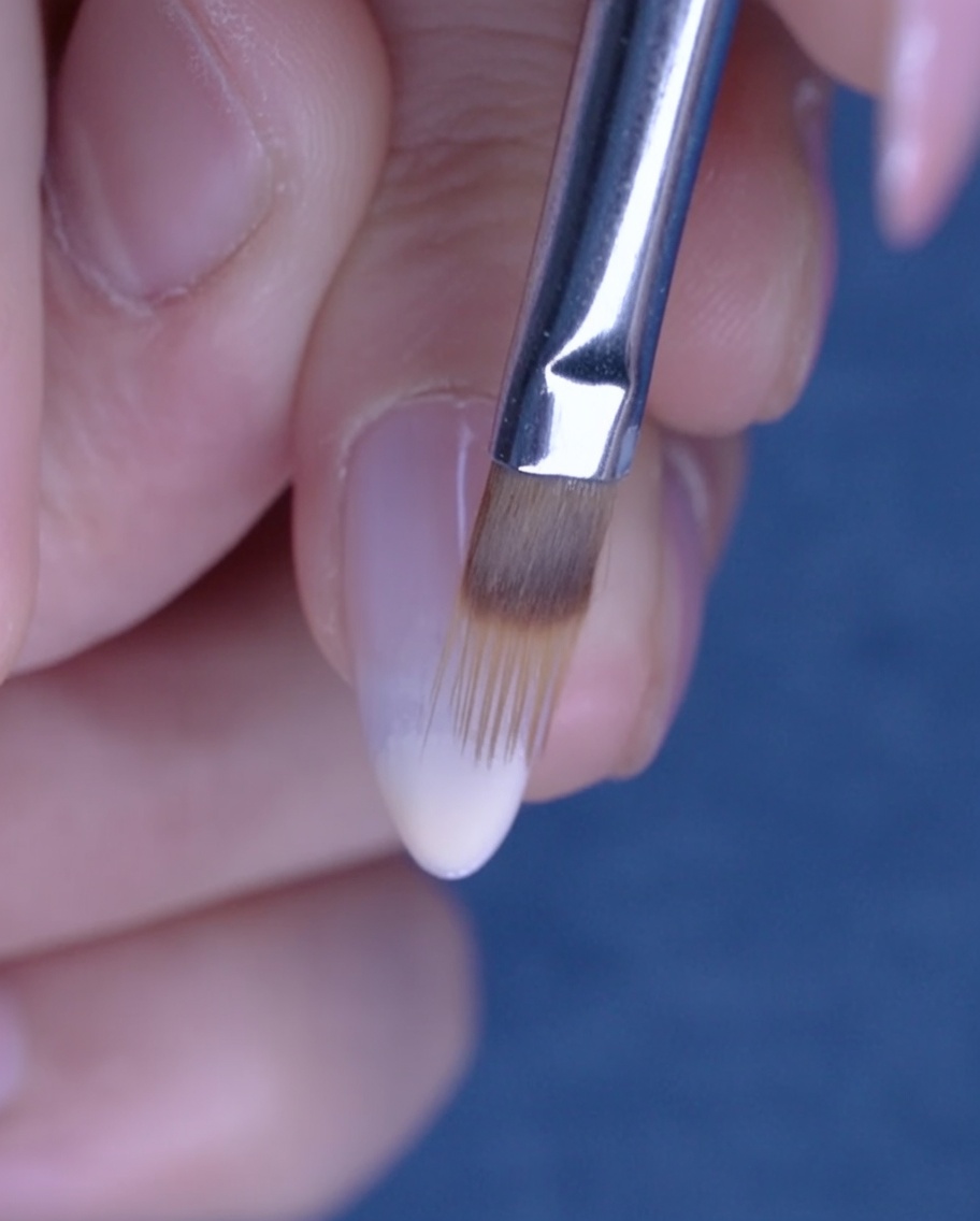 Ein flacher Pinsel verblendet Nude-Gel nach oben auf dem Nagel für einen Ombre-Effekt.