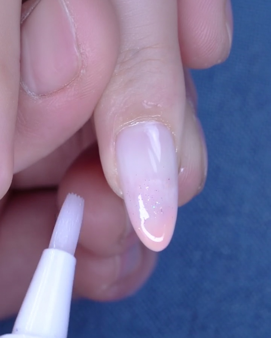 Ein Nagelölstift wird verwendet, um Öl auf die hydratisierte Haut um einen frisch manikürten Nagel aufzutragen.