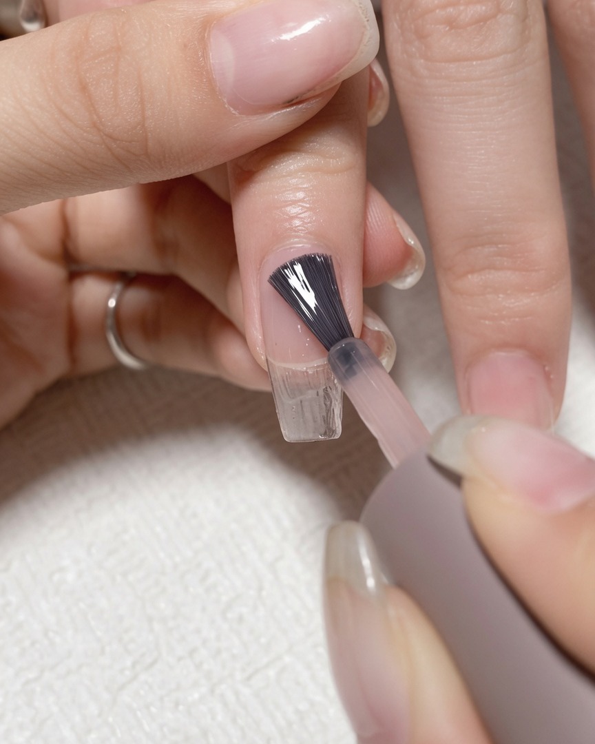 Ein Pinsel trägt klares Base Coat Gel auf einen sauberen Naturnagel auf.