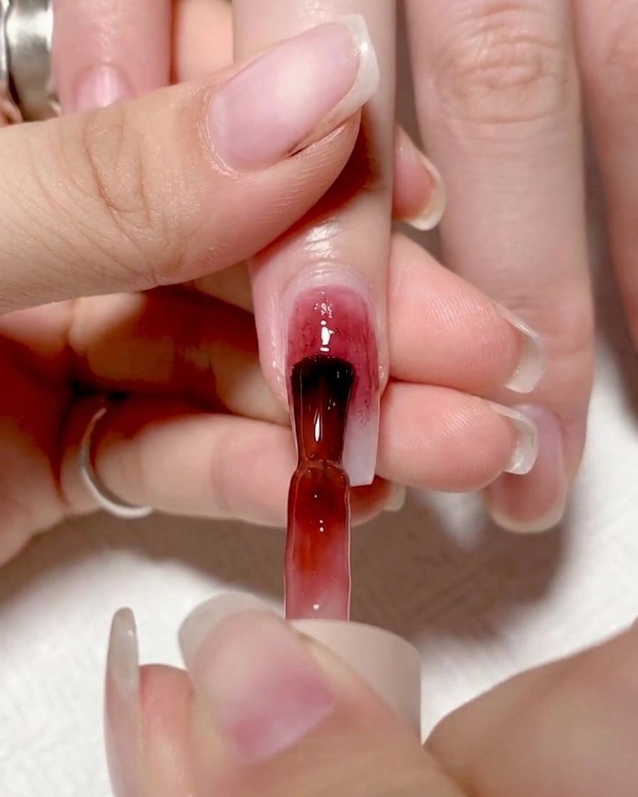 Ein Pinsel trägt ein leuchtend rotes Gel auf die linke Hälfte eines Fingernagels auf und erzeugt so einen Farbblock.