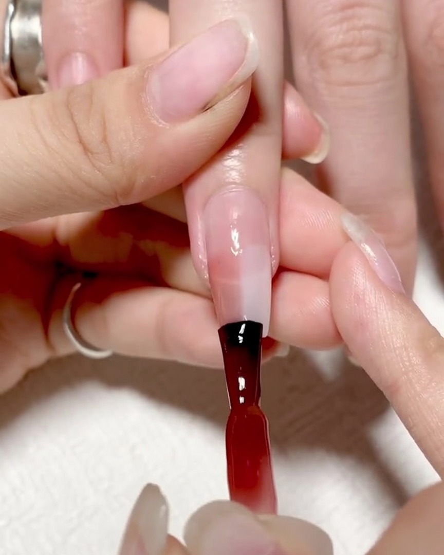 Ein Ombré-Pinsel tupft auf die Mitte des Nagels, wo rotes und klares Gel aufeinandertreffen, um die Linie weicher zu machen.