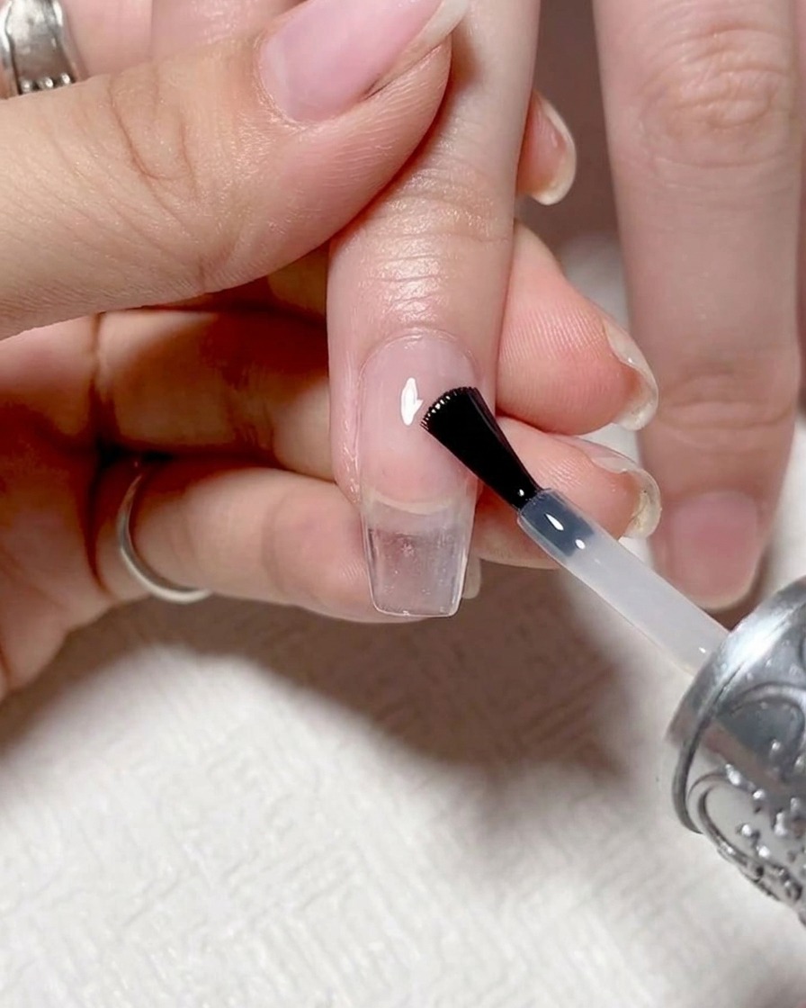 Nahaufnahme eines Nagelpinsels, der einen klaren, glänzenden Top Coat auf einen fertigen Ombré-Nagel aufträgt.