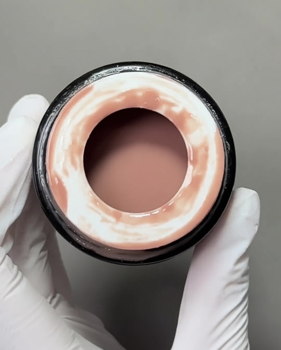 Nahaufnahme eines flachen Gel-Pinsels, der eine nude-farbene Basis auf eine Nagelspitze aufträgt.