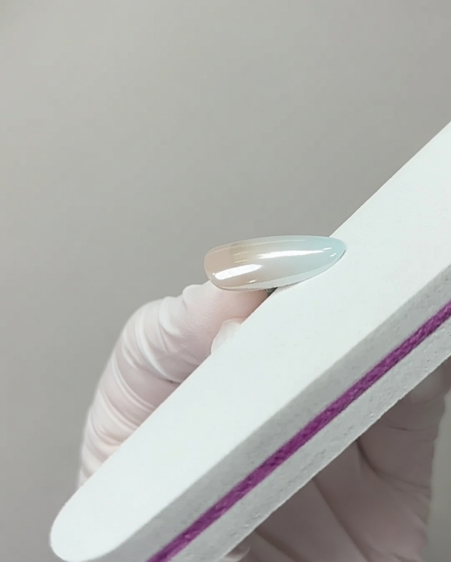Eine Nagelfeile berührt leicht die freie Kante eines chrombeschichteten Nagels, um überschüssiges Pigment zu entfernen.