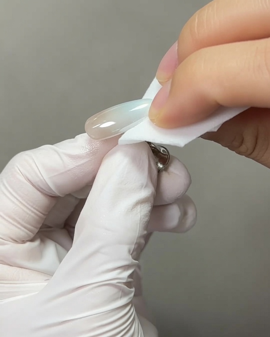 Ein Nagelpinsel trägt einen klaren Tropfen Aufbaugel auf die Spitze eines fertigen Chrom-Nagels auf.