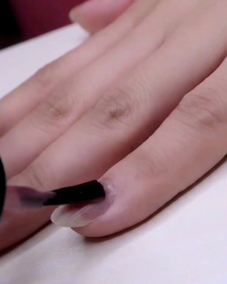 Ein Pinsel trägt transparenten rosa Jelly-Lack auf den gesamten kleinen Fingernagel auf.