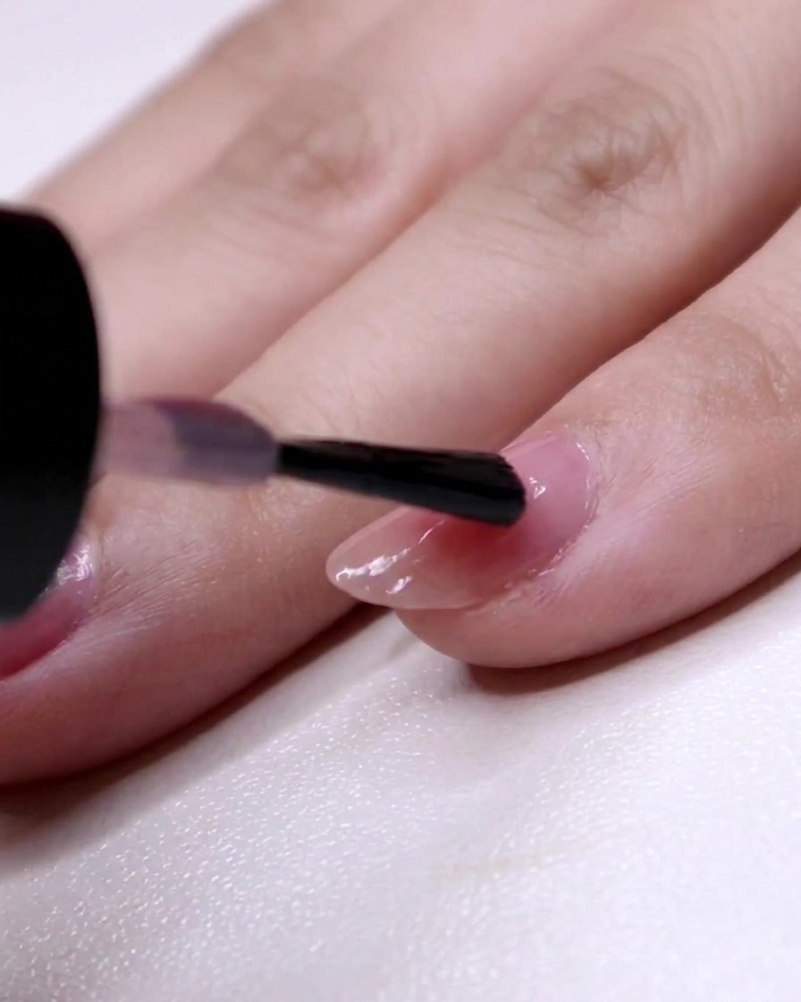 Ein Nagelpinsel malt die zweite Schicht rosa Lack ab der Zwei-Drittel-Markierung bis zur Spitze des Ringfingers.
