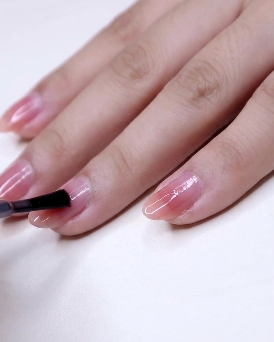 Nahaufnahme eines Pinsels, der rosa Lack von der Mitte bis zur Spitze eines Fingernagels aufträgt.