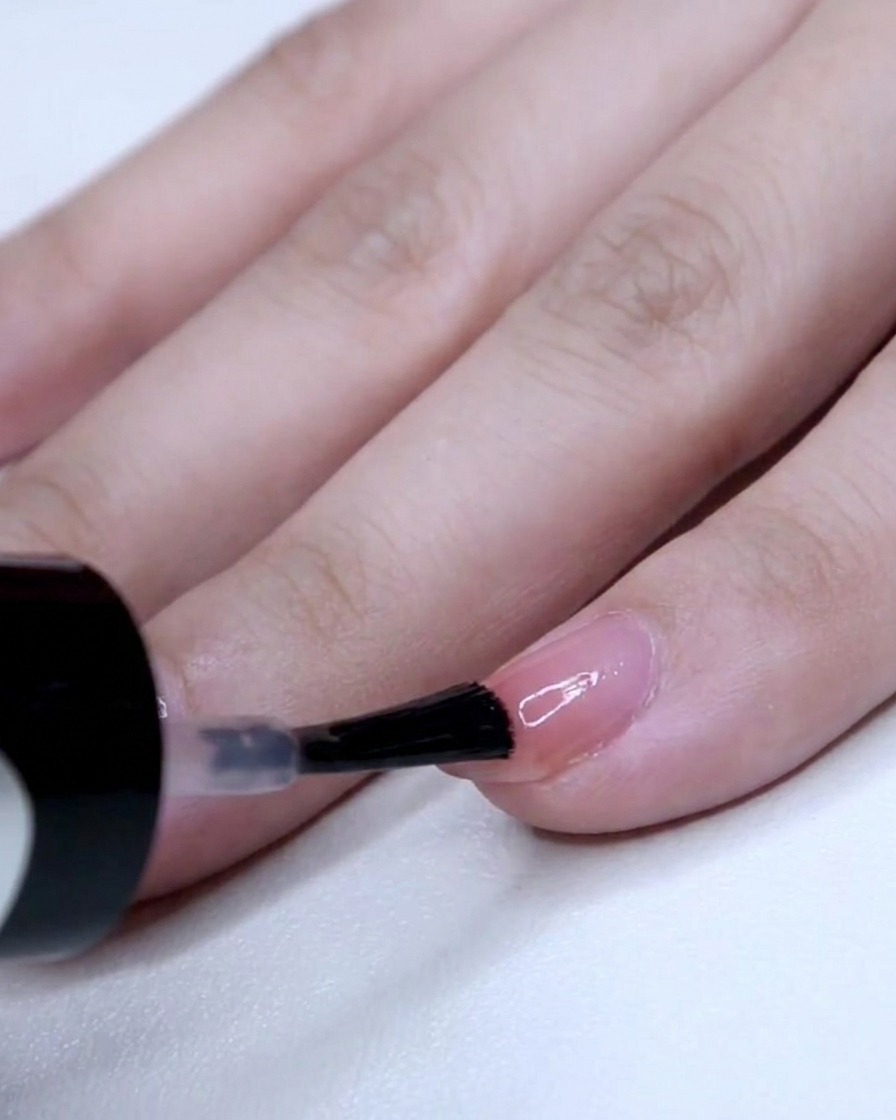 Ein Nagelpinsel trägt eine konzentrierte Schicht rosa Lack auf die Spitze eines kleinen Fingernagels auf.