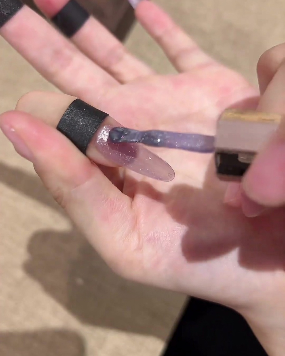 Ein Nagelpinsel trägt einen finalen, glänzenden Top Coat auf das fertiggestellte Galaxie-Cat-Eye-Nageldesign auf.