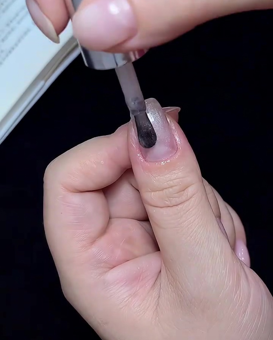 Ein Pinsel trägt halbtransparenten weißen Cat-Eye-Gellack auf einen Fingernagel auf.