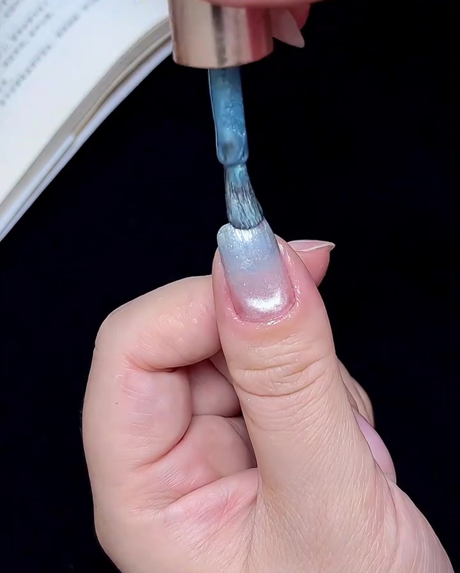 Ein Pinsel trägt eine kleine Menge blaues Gel auf die Nagelspitze auf.