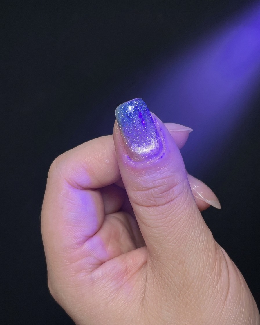 Eine Hand wird unter dem violetten Licht einer UV/LED-Nagellampe zum Aushärten positioniert.