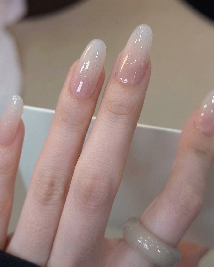 Ein Pinsel trägt einen klaren, glänzenden Top Coat über dem fertigen Milky White Gradient Nail auf.