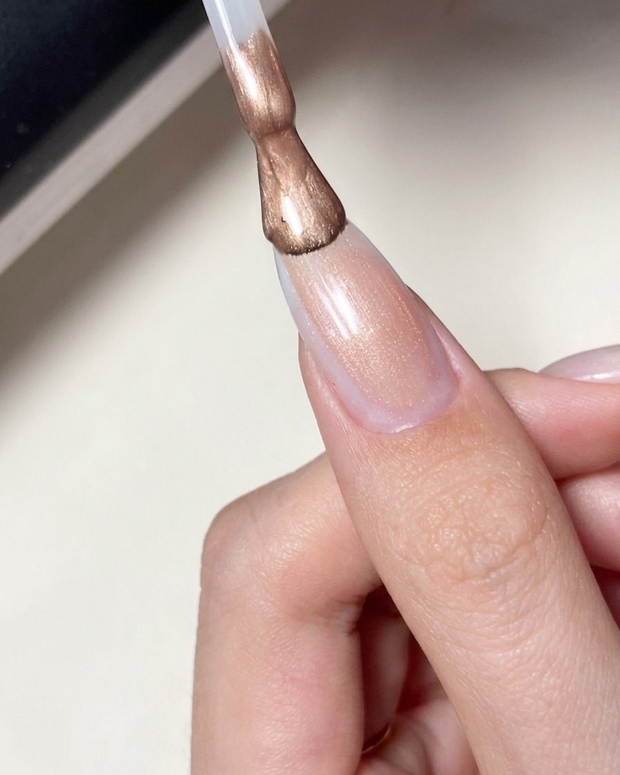 Ein Pinsel trägt einen milchig-rosafarbenen, transparenten Gellack auf einen Nagel mit Stern-Design auf.