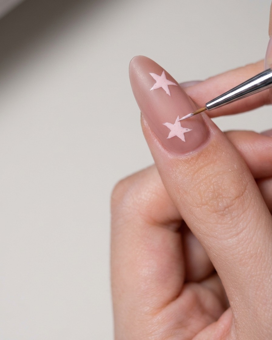 Ein kleines Werkzeug trägt weiße Nailart-Paste auf, um die Sternform auf dem Nagel auszufüllen.
