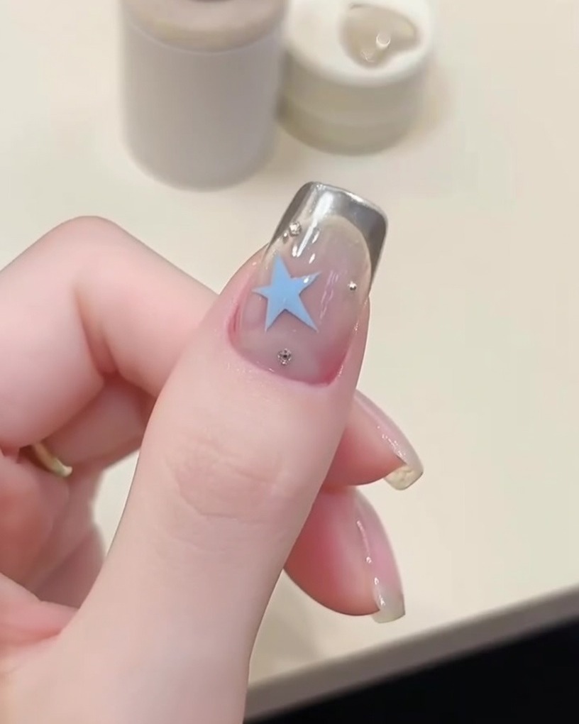 Ein Schwämmchenapplikator reibt silbernes Chrome-Puder über eine Schablone auf die Nagelspitze.