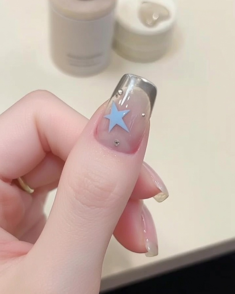Nahaufnahme eines feinen Liner-Pinsels beim Malen eines blauen Sterns auf einem Nagel.