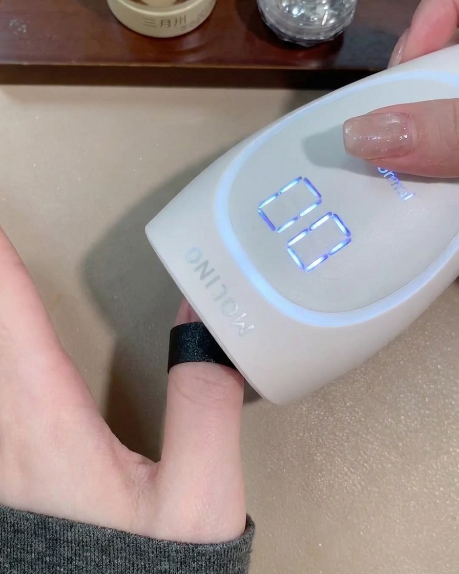 Eine Hand in einer matten, weißen tragbaren Nagellampe beim Aushärten des Cat-Eye-Gels.