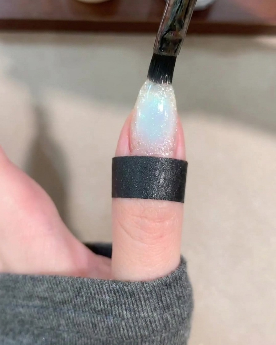Ein Gel-Pinsel trägt eine Schicht klaren Base Coat über den dekorierten Nagel auf.