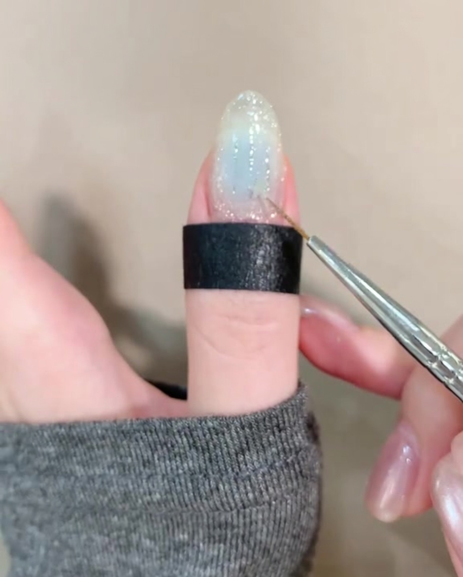 Eine Pinzette platziert eine kleine, glänzende goldene sternförmige Paillette auf einem klaren Nagel.