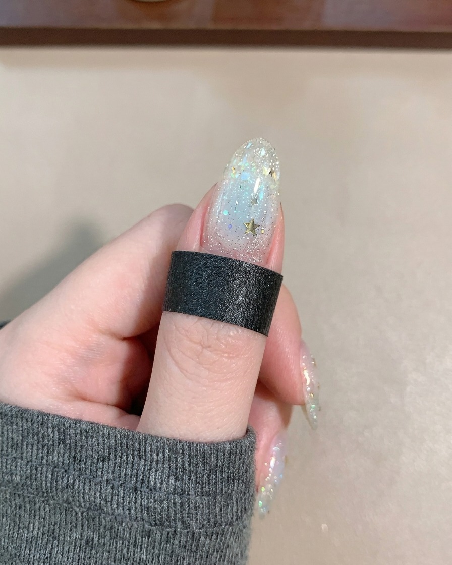 Ein Pinsel trägt klaren, glänzenden Top Coat über einen mit Sternen und Linien dekorierten Nagel auf.