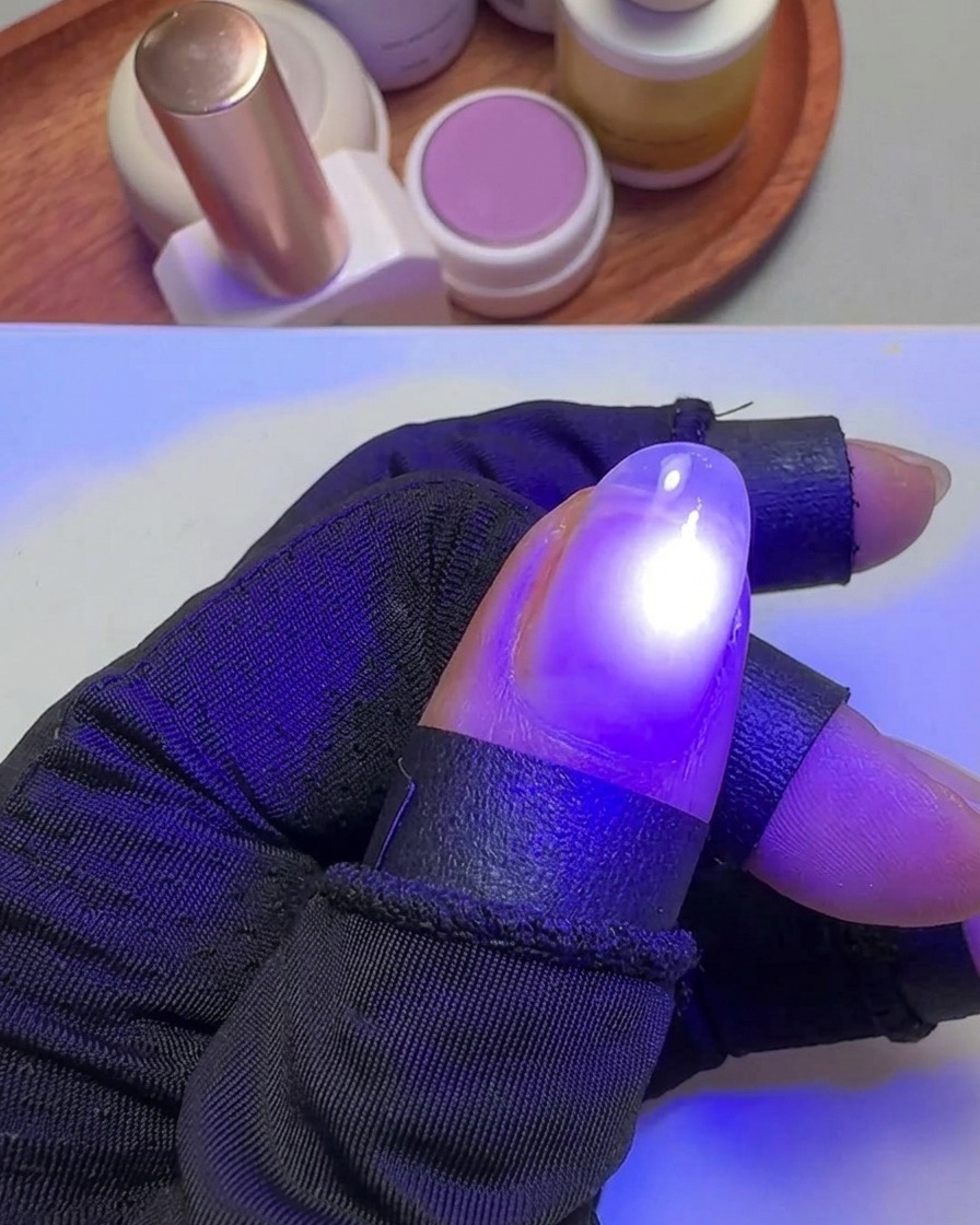 Ein Daumen wird unter das gezielte violette Licht einer kleinen UV-Lampe gehalten, um den Gellack auszuhärten.
