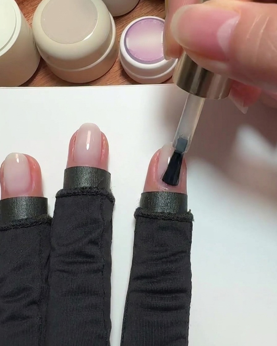 Ein Pinsel trägt einen transparenten, pinken Nude-Gellack auf einen Zeigefingernagel auf.