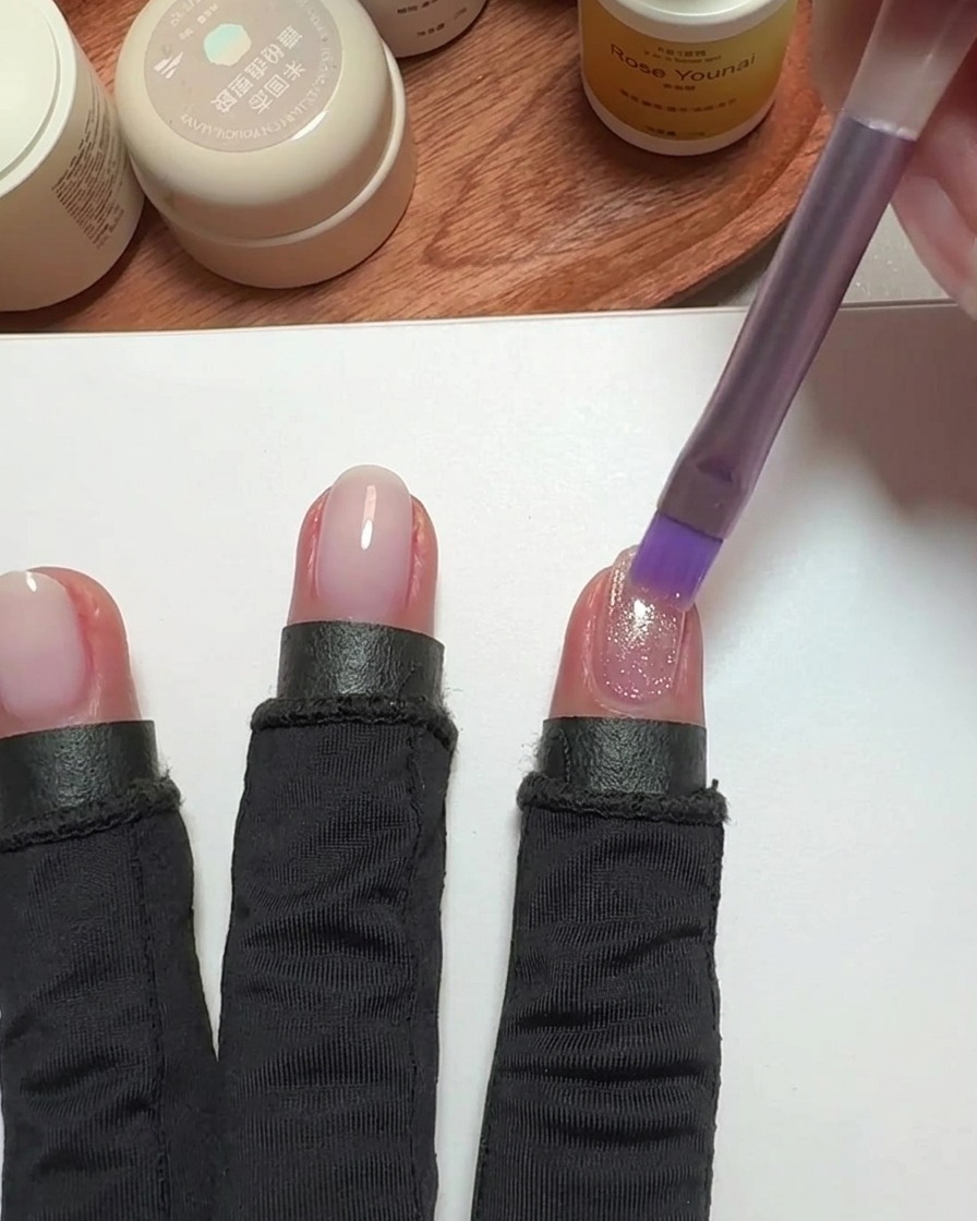 Ein Pinsel trägt pinken Cat-Eye-Lack auf einen Fingernagel auf.