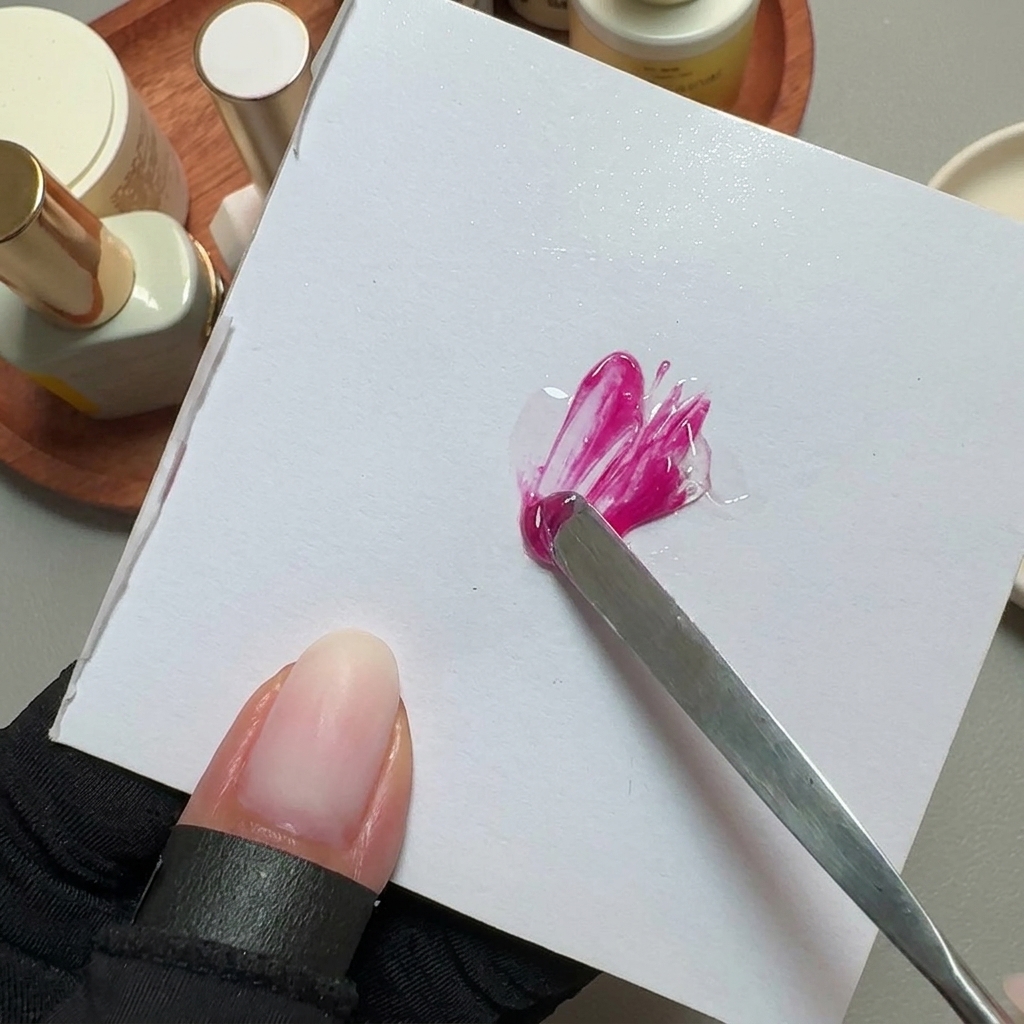 Ein Metallspatel mischt leuchtend pinken Gellack auf einer weißen Mischpalette.