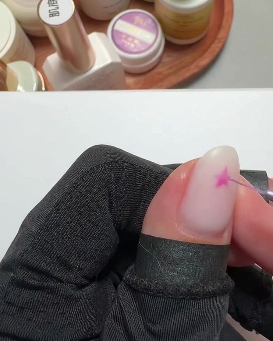 Nahaufnahme eines feinen Liner-Pinsels, der einen leuchtend pinken Stern auf eine milchig-weiße Basis malt.