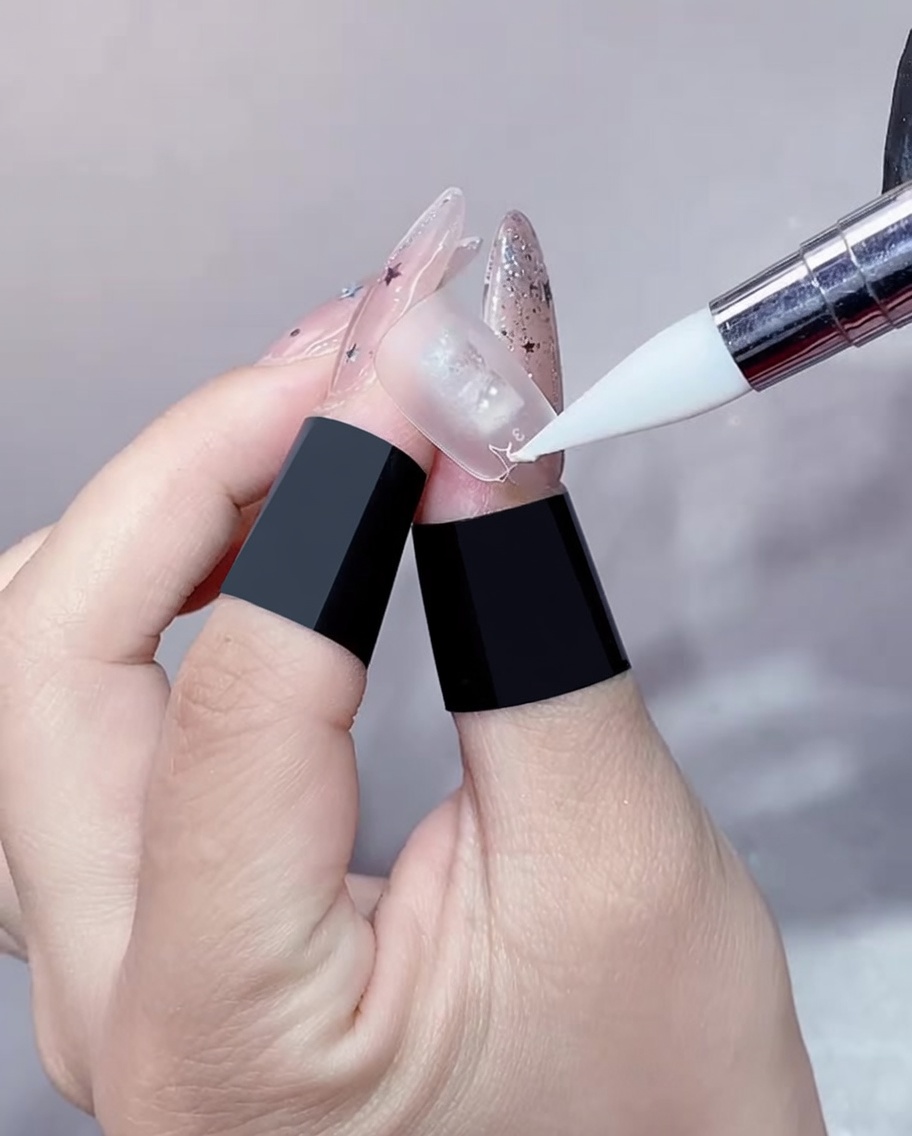 Nahaufnahme einer Gel-Pinselspitze, die ein klares Gel auf den Rand einer Nagelverlängerung aufträgt.