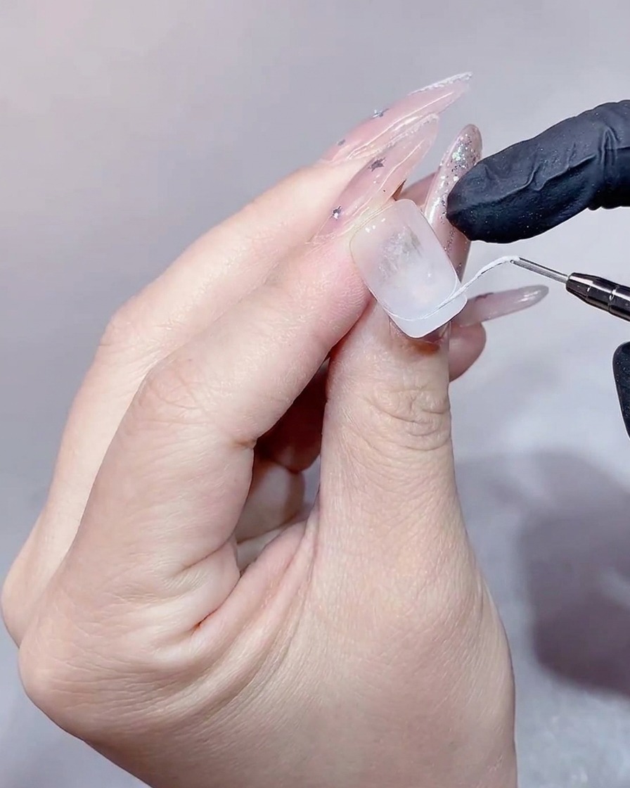 Ein flacher Pinsel füllt den Bereich der French-Spitze mit weißem Gel aus.