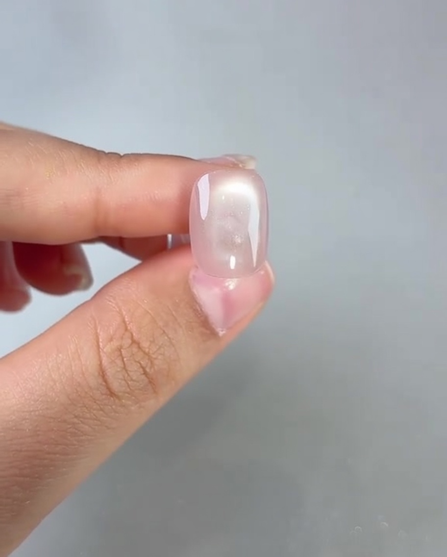 Ein Pinsel trägt einen klaren Top Coat auf einen ausgehärteten rosa Cat-Eye-Nagel auf.