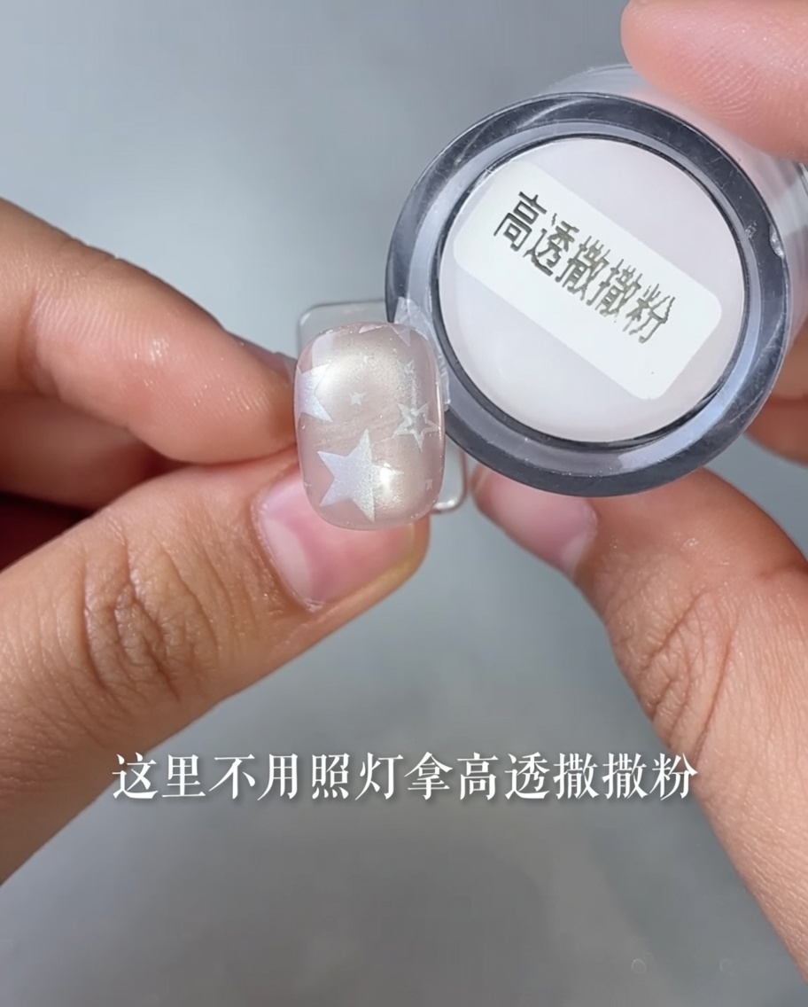 Nahaufnahme eines Fingernagels mit einem Sternendesign, der in einen kleinen Behälter mit transparentem Puder getaucht wird.