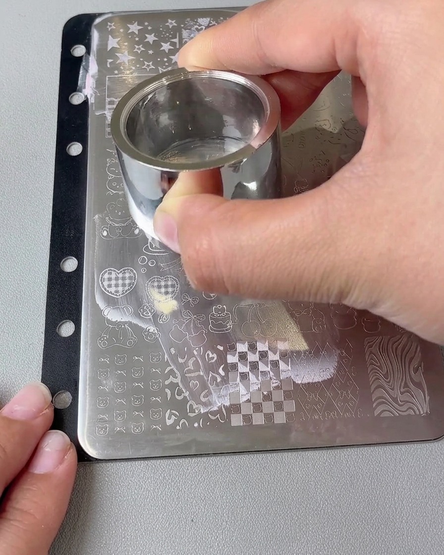 Nahaufnahme eines großen Stempelkopfes mit einem übertragenen Herzdesign, das auf einen Nagel gedrückt wird.