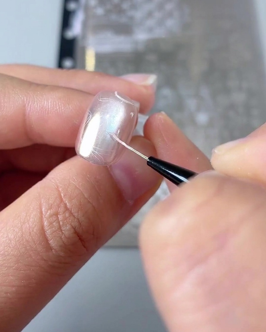 Nahaufnahme, die zeigt, wie ein feiner Liner-Pinsel die Details eines gestempelten Herzdesigns auf einem Nagel ausfüllt.