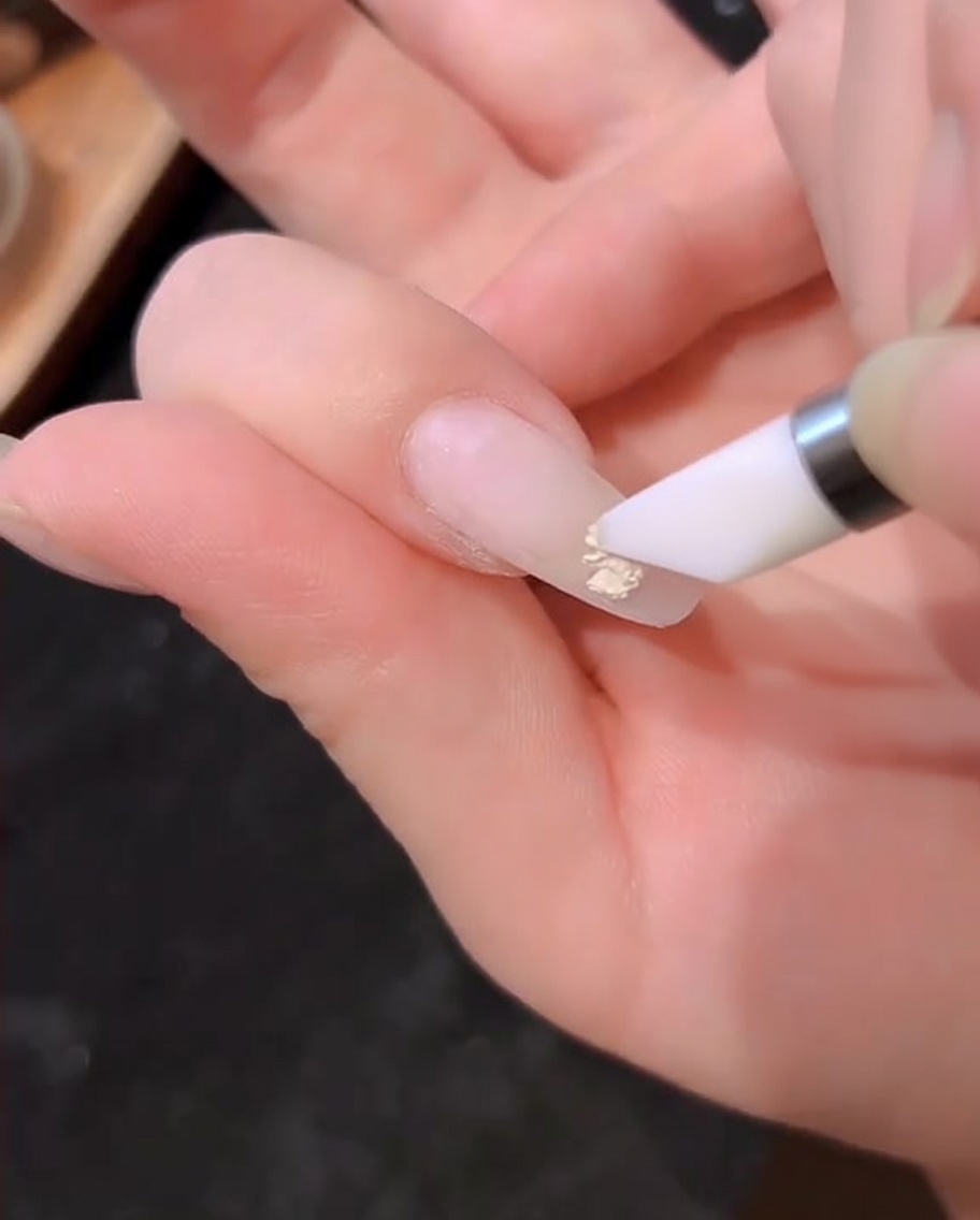 Ein Gel-Pinsel trägt eine Schicht milchig-weißes Gel auf einen Naturnagel auf.