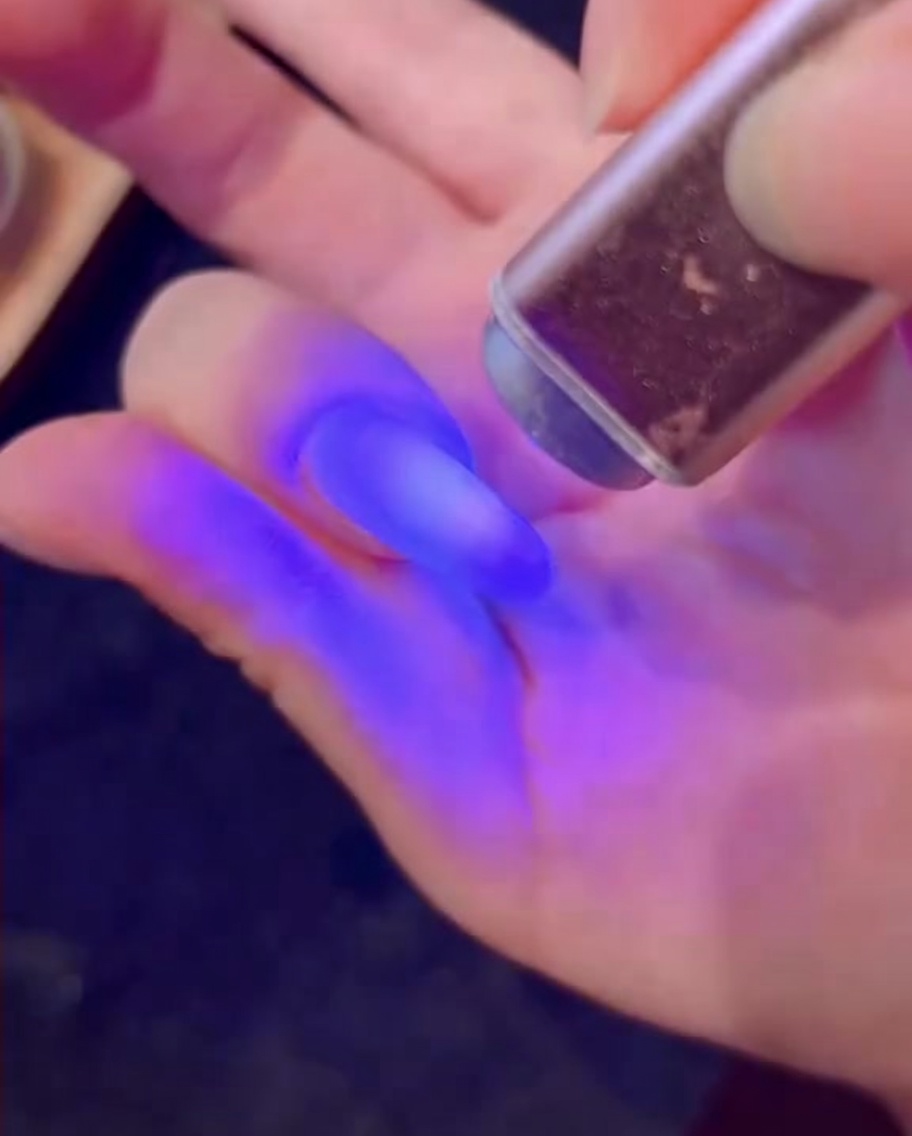 Ein Pinsel trägt weißes Gel mit diamantartigem Glitzer auf einen Nagel auf.