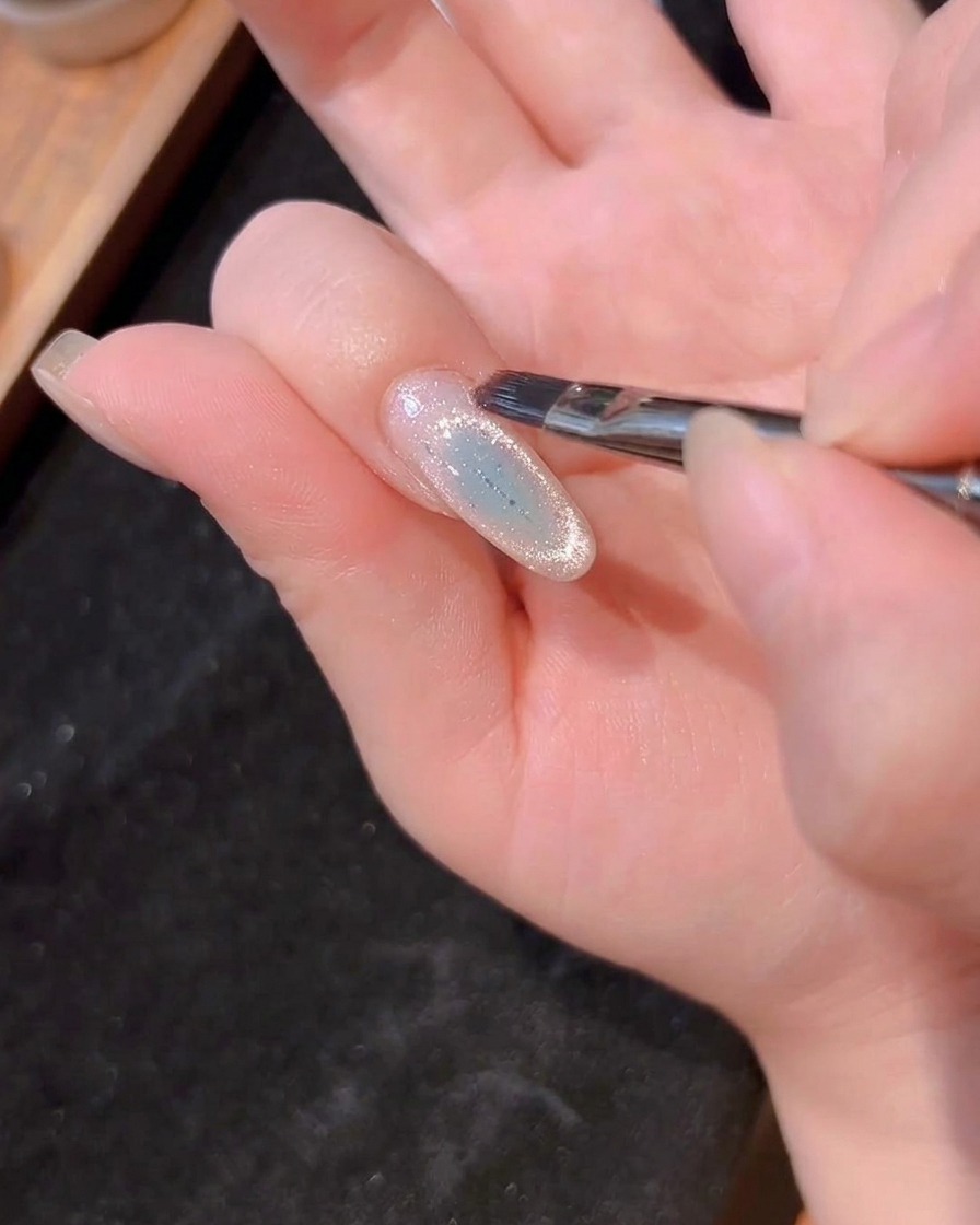 Ein Nagelpinsel trägt eine dünne, klare Schicht Builder-Gel auf den gesamten Nagel auf.