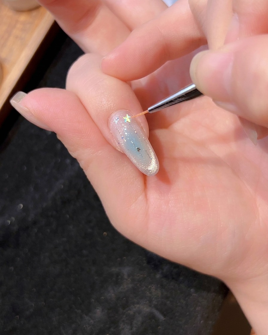 Ein feiner Pinsel platziert einen holografischen Stern auf das feuchte Gel des Nagels.