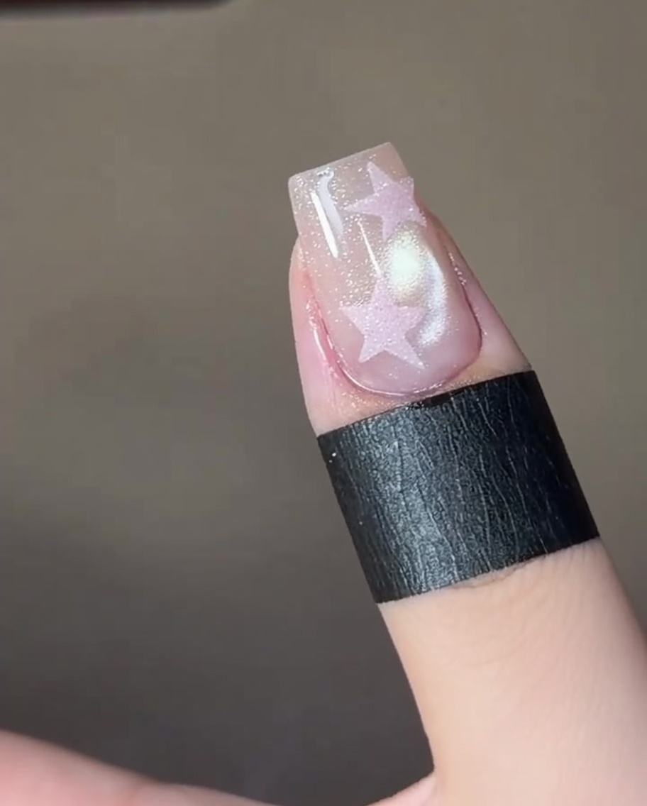 Eine Pinzette platziert einen Stern-Sticker auf einem manikürten Fingernagel.
