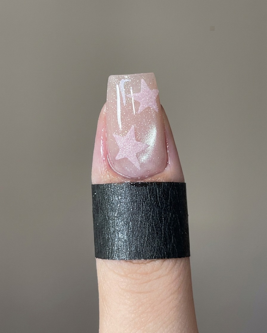 Ein feiner Nail-Art-Pinsel füllt eine Stern-Schablone auf einem Nagel mit rosa Gel.