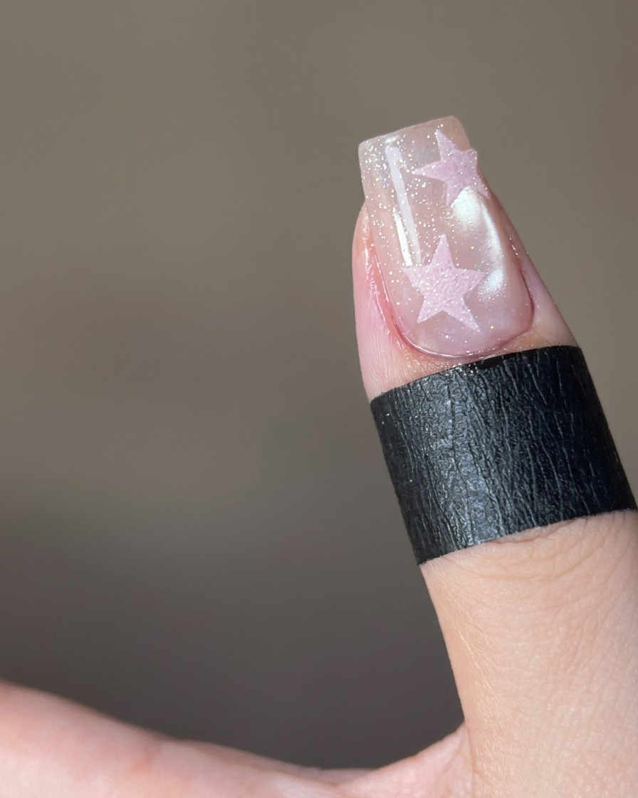 Nahaufnahme, wie rosa Zuckerpuder auf ein sternförmiges Design auf einem Nagel gestreut wird.