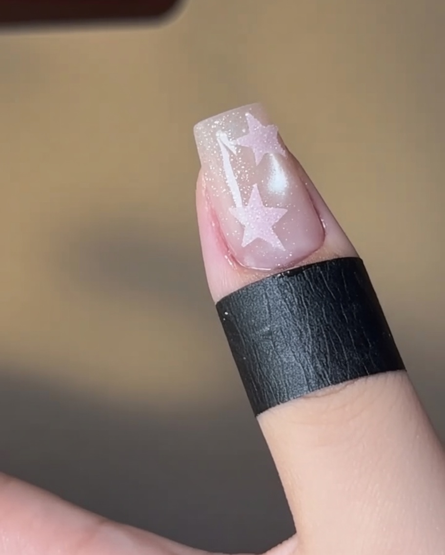 Ein Nagel mit einem rosa ausgefüllten Sterndesign härtet unter einer Lampe.