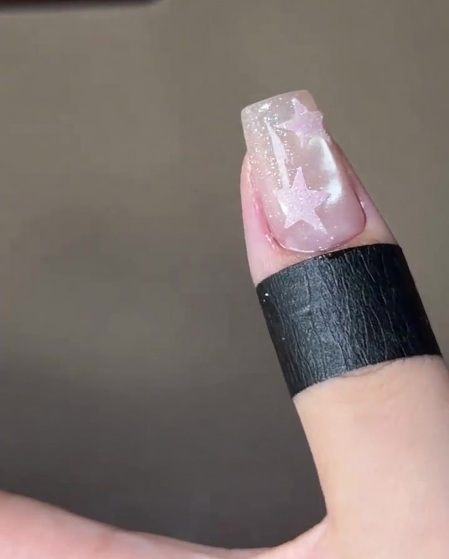 Nahaufnahme, wie ein Pinsel einen klaren Top Coat über einen rosa Stern auf einem schimmernden Nagel aufträgt.