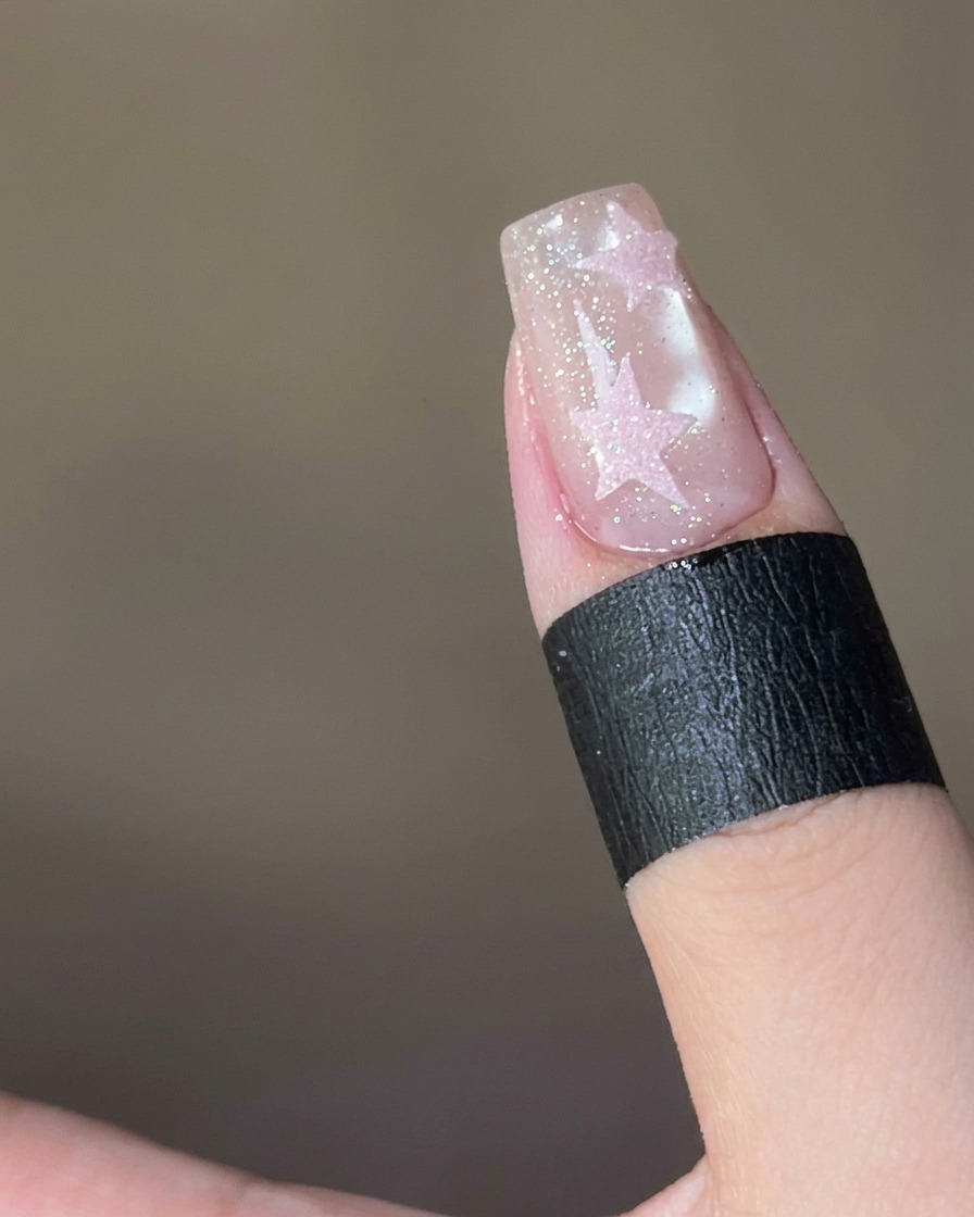 Rosa Zuckerpuder wird auf einen mit feuchtem Top Coat bedeckten Stern auf einem Nagel gestreut.