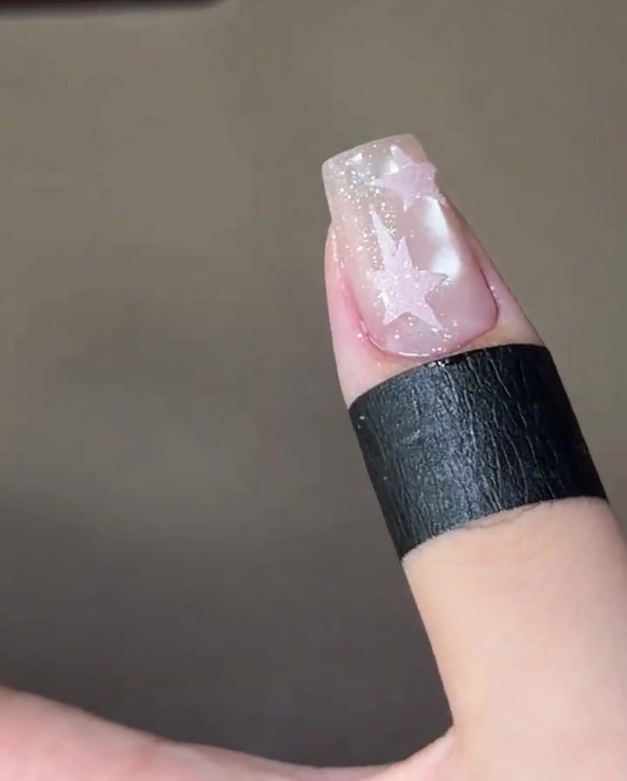 Ein fertiger Nagel mit zwei texturierten rosa Zuckersternen härtet in einer UV-Nagellampe.