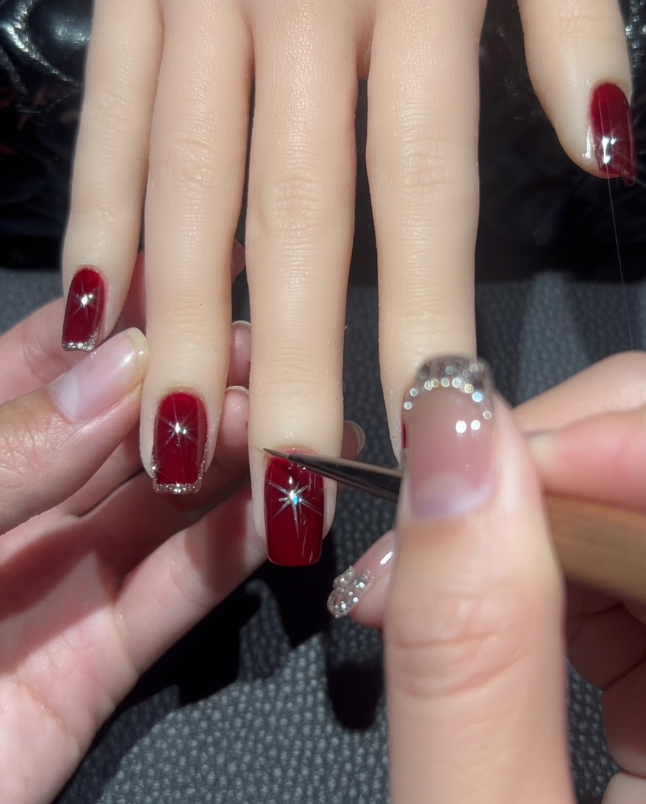 Nahaufnahme eines Liner-Pinsels, der eine dünne Linie aus Roségold-Glitter um den Rand eines dunkelroten Nagels zieht.