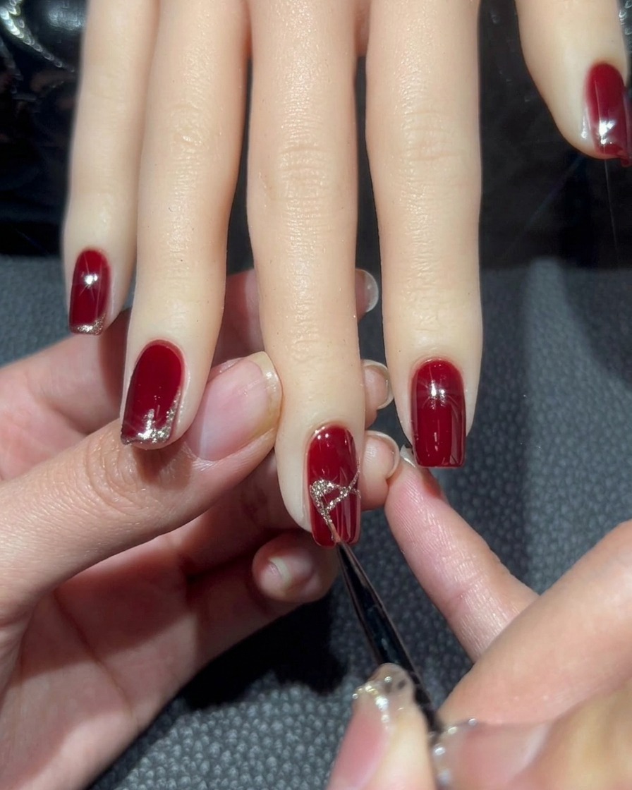 Nahaufnahme des Mittelfingernagels, bei dem das X mit dichtem Roségold-Glitter zu einer Schleifenform ausgefüllt wird.